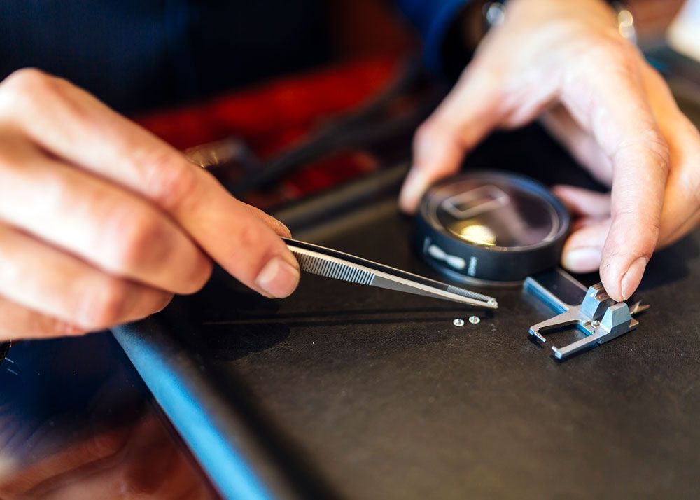 Closeup of a jeweler's hands as he picks up a diamond from a tray with a long pair of tweezers.