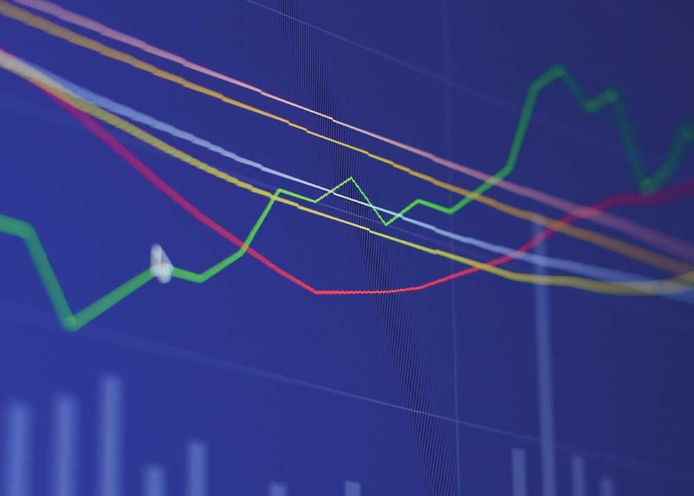 A stock market line graph showing some lines rising others falling and others flat on a blue screen